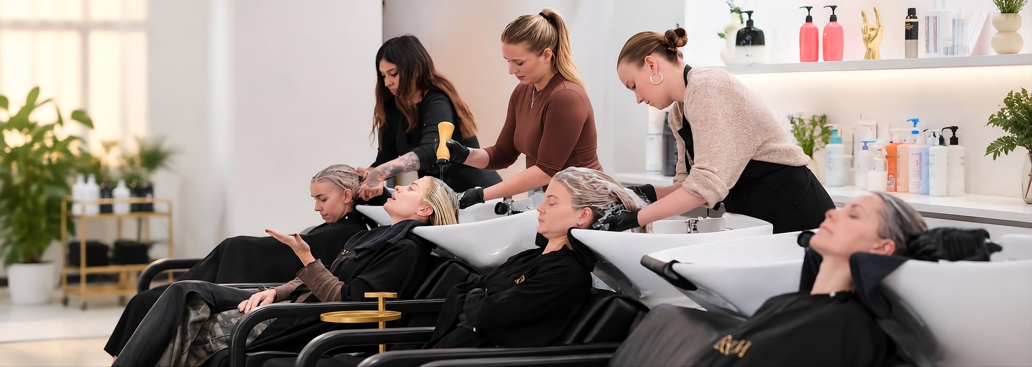 A row of salon backwash chairs with stylists at work